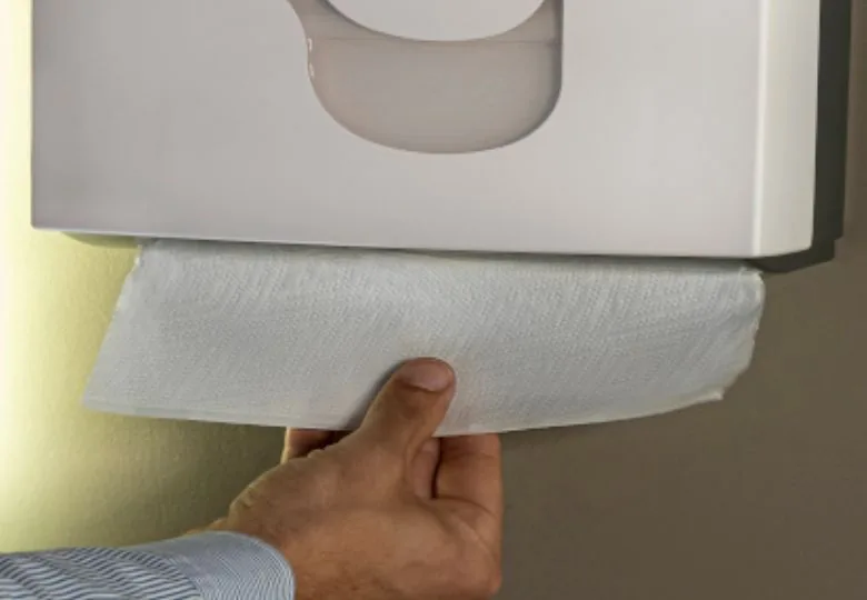 Une main tire un essuie-mains d'un distributeur blanc